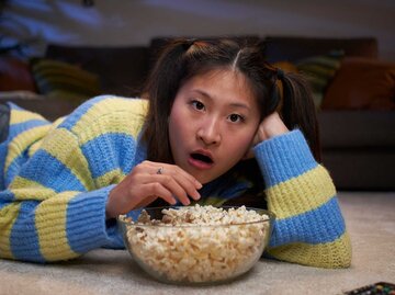 Junge Frau schaut einen Film und isst Popcorn. | © Getty Images/Carlos Barquero
