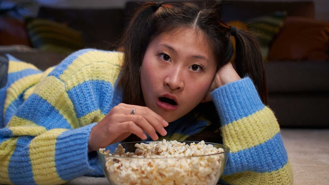 Junge Frau schaut einen Film und isst Popcorn. | © Getty Images/Carlos Barquero