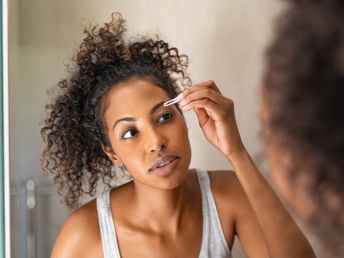 Frau zupft sich die Augenbrauen vor dem Spiegel | © Getty Images/Ridofranz