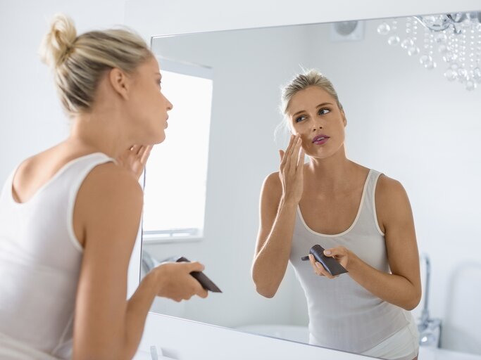 Frau trägt vor dem Spiegel eine Gesichtscreme auf | © Getty Images/Letizia Le Fur