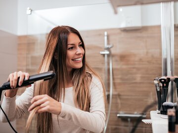 Frau glättet sich die Haare | © Getty Images/nortonrsx