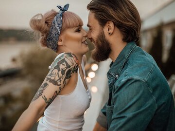 Mann mir Bart steht vor Frau mit Tattoos und schaut sie verliebt an. | © Getty Images / Anchiy