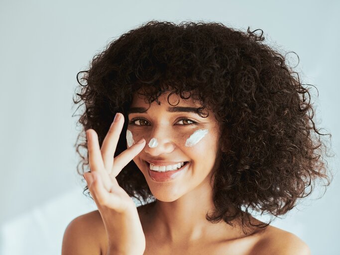 Eine junge Frau cremt sich das Gesicht mit Sonnencreme ein | © GettyImages/Delmaine Donson