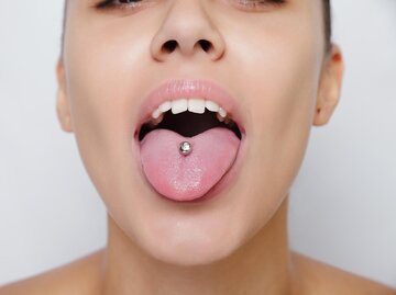 Frau streckt Zunge mit Piercing raus | © Getty Images/MishaBeliy