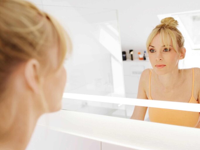 hübsche, junge Frau betrachtet sich im Spiegel | © Getty Images/Westend61