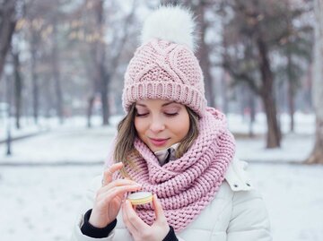 Frau mit rosa Mütze und Schal benutzt Lippenpflege im Winter | © Getty Images/petrunjela