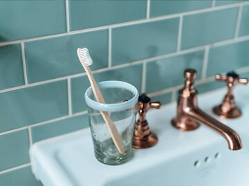 Zahnbürste in Becher steht auf Waschbecken | © Getty Images/Oscar Wong