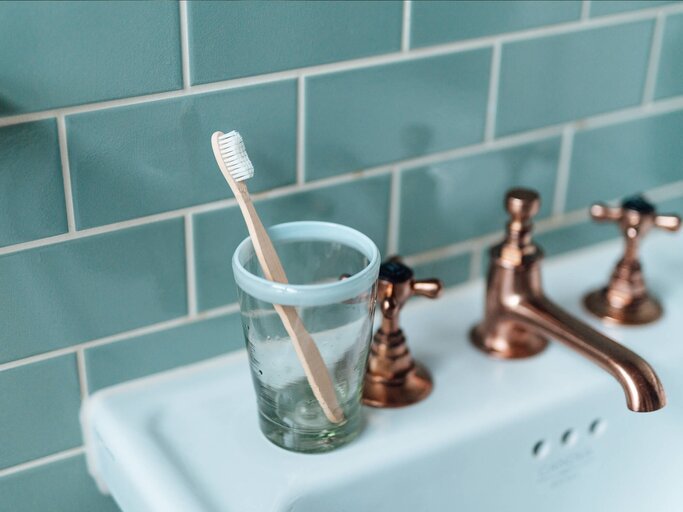 Zahnbürste in Becher steht auf Waschbecken | © Getty Images/Oscar Wong