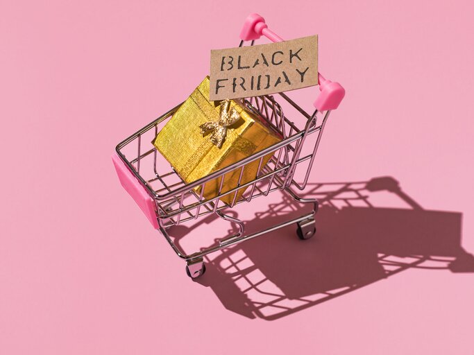 Symbolbild mit Einkaufswagen, Schild "Black Friday" und Geschenk darin | © Getty Images/DBenitostock