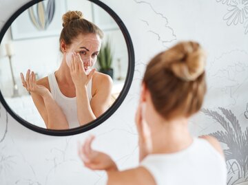 Frau steht vor dem Spiegel und cremt sich das Gesicht ein | © Getty Images/Sergey Mironov