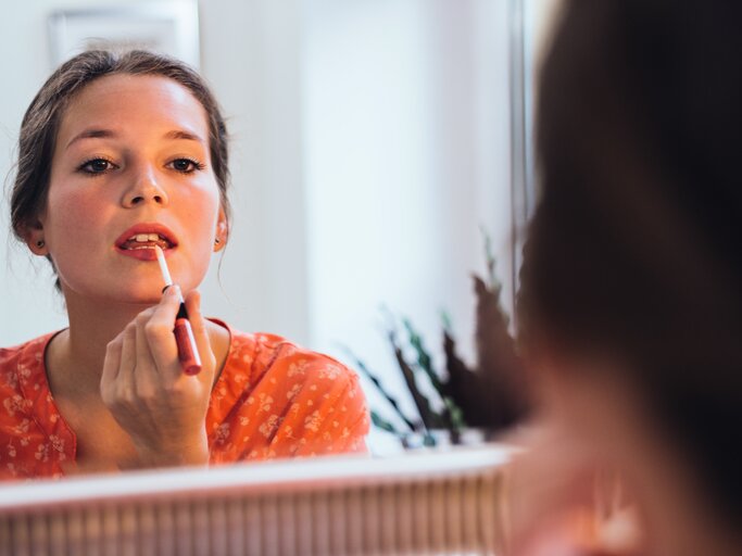 Frau trägt vor dem Spiegel Lippenstift auf | © Getty Images/Guido Mieth