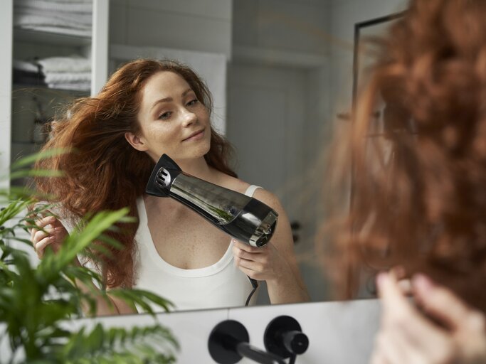 Frau föhnt sich die Haare vor dem Spiegel | © Getty Images/Anna Bizon / EyeEm