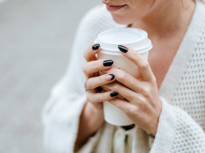 Frau mit schwarzen Fingernägeln hält einen Kaffeebecher ToGo. | © Getty Images / F.J. Jimenez