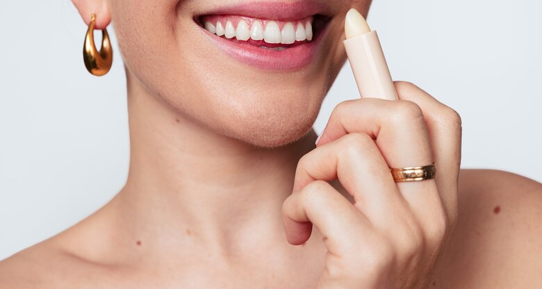 Lachende Frau pflegt Lippen mit Lip Balm | © AdobeStock/kegfire