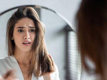 Porträt einer gestressten jungen Frau mit einem Bündel gefallener Haare in der Hand | © Getty Images/Prostock-Studio