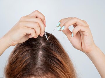 Frau mit braunen Haaren zupft sich mit Pinzette graue Haare aus | © Getty Images/inside-studio