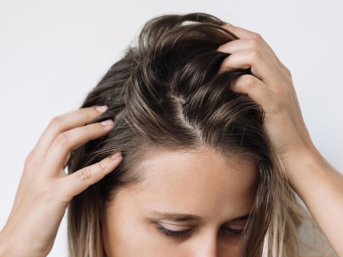 Frau fasst sich mit den Fingern in den strähnigen Haaransatz | © AdobeStock/Марина Демешко