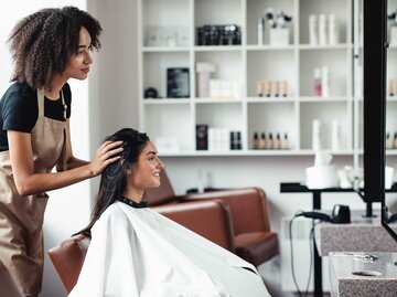 Junge Frau sitzt im Friseursalon und bespricht mit ihrer Friseurin eine neue Frisur. | © Adobe Stock/Prostock-studio