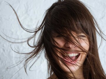 Brünette Frau wirft lachend ihre langen Haare umher. | © Getty Images/Xsandra