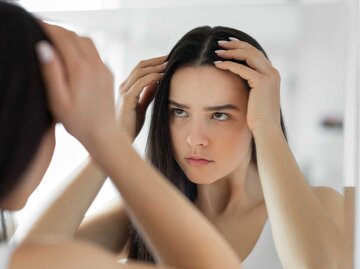 Brünette Frau sucht vor dem Spiegel nach einem grauen Haar. | © Getty Images/bymuratdeniz
