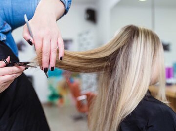 Junger Frau werden die Haare beim Friseur geschnitten | © Getty Images/Group4 Studio