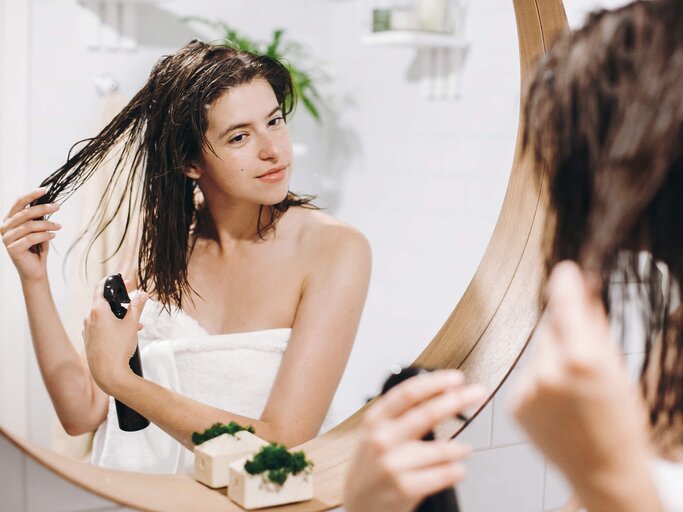 Frau steht vor dem Spiegel und kämmt sich die Haare | © Getty Images/Bogdan Kurylo