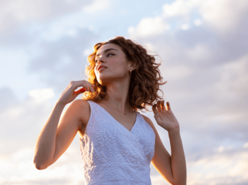 Frau mit Locken tanzt unter blauem Himmel | © Getty Images/Cavan Images