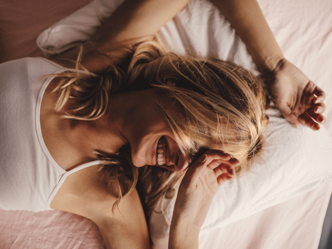 Blonde Frau liegt im Bett und lacht | © Getty Images/AleksandarNakic