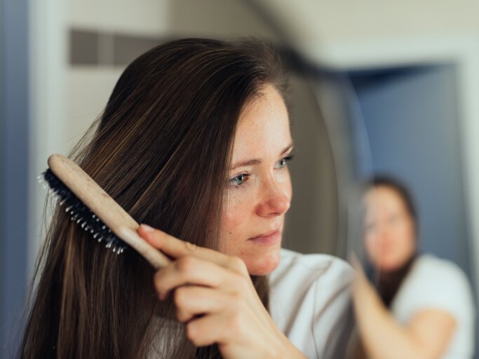 Brünette Frau kämmt sich die Haare | © Getty Images/Guido Mieth