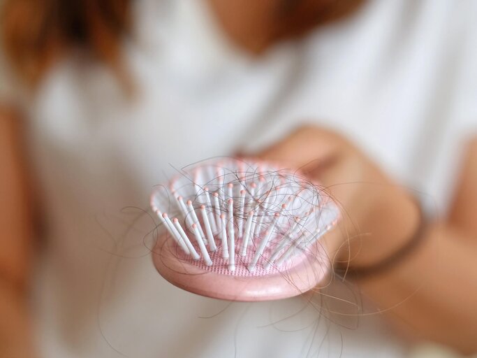 Frau hat Haarausfall und zeigt rosa Bürste mit Haaren drin | © Getty Images/Chalisa Thammapatanakul / EyeEm