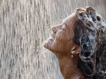 Glückliche Frau mit Shampoo im Haar steht unter der Dusche. | © Getty Images / skynesher