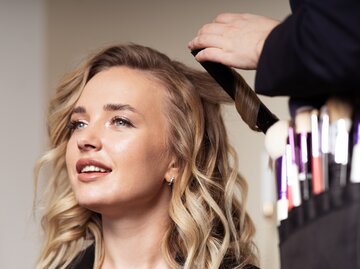 Junger Frau werden die Haare mit einem Lockenstab gestylt | © Getty Images/spb2015