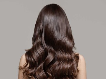 Frau mit langen, glänzenden Haaren steht mit dem Rücken zur Kamera | © Adobe Stock/yuriyzhuravov