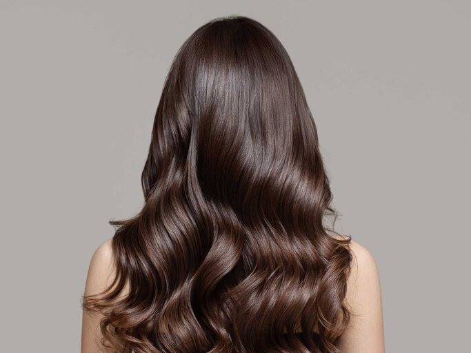 Frau mit langen, glänzenden Haaren steht mit dem Rücken zur Kamera | © Adobe Stock/yuriyzhuravov