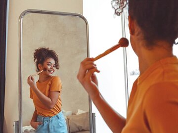 Frau schminkt sich vor Spiegel. | © Getty Images/Dasha Petrenko/EyeEm