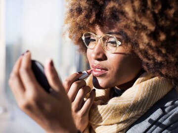 Frau trägt Lippenstift mit Handspiegel auf | © Getty Images/Cavan Images