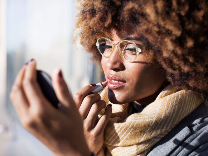 Frau trägt Lippenstift mit Handspiegel auf | © Getty Images/Cavan Images