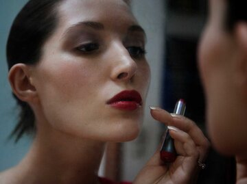 Frau trägt Lippenstift vor dem Spiegel auf | © Getty Images/Cavan Images