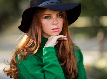 Sonnenschein junge lächelnde Frau mit roten lockigen Haaren trägt grünen Pullover im Herbstpark | © GettyImages/_chupacabra_