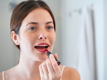 Person mit Sommersprossen trägt Lippenstift auf | © Getty Images/Mindful Media
