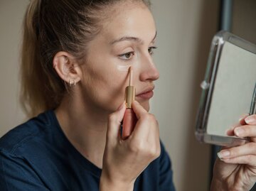 Frau, die Concealer unter den Augen aufträgt | © Getty Images/DGLimages