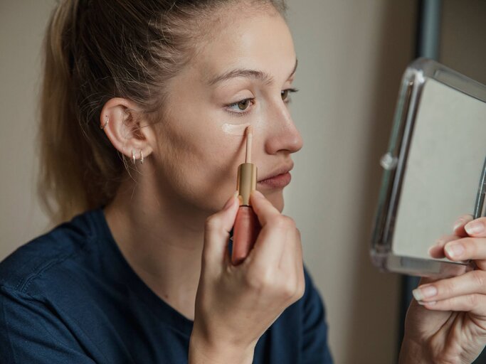 Frau, die Concealer unter den Augen aufträgt | © Getty Images/DGLimages