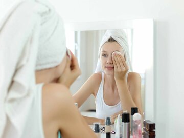 Hübsche junge Frau schaut in den Spiegel und reinigt ihr Gesicht | © Getty Images/bymuratdeniz
