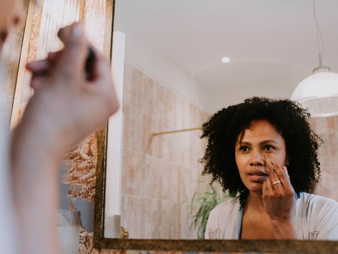 Frau trägt in Spiegel Concealer auf | © Getty Images/Catherine Falls Commercial