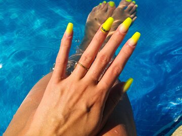 Eine Hand mit gelb lackierten Nägeln über einem Pool | © Getty Images/mikroman6