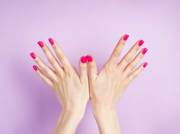 Hände mit pinkem Nagellack vor lila Hintergrund | © Getty Images/Volodymyr Bushmelov
