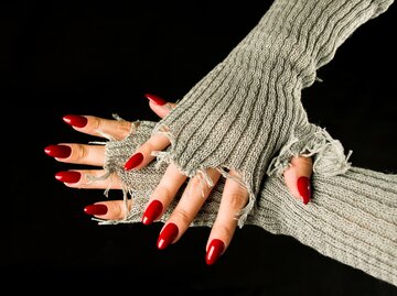 Frauenhand mit spitzen, roten Nägeln auf schwarzem Hintergrund | © Getty Images/Anton Deev