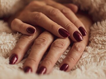 Rot lackierte Fingernägel zwischen einer Felldecke | © Adobe Stock/juste.dcv