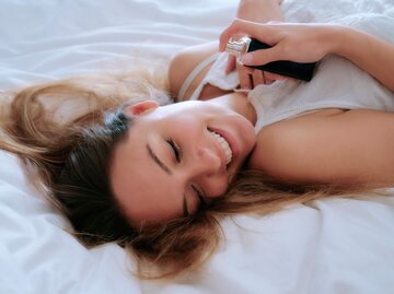 Frau liegt glücklich im Bett mit einem Parfum in der Hand | © Getty Images/John Slater