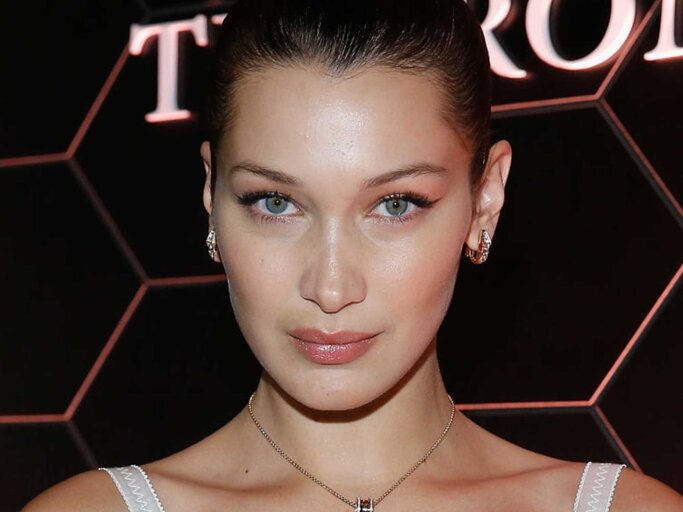 Model Bella Hadid schaut in die Kamera. Sie trägt ein weißes Kleid und ihre Haare hochgesteckt | © Getty Images/John Lamparski 